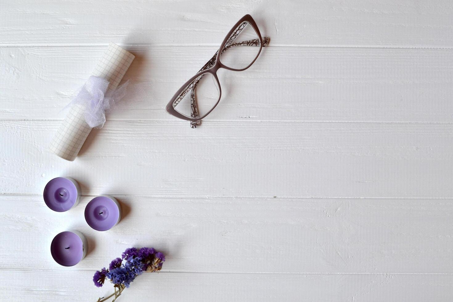Letter, glasses, candle and flower on the white table. Beutiful female objects on the white wooden background. Flat lay in violet color. photo