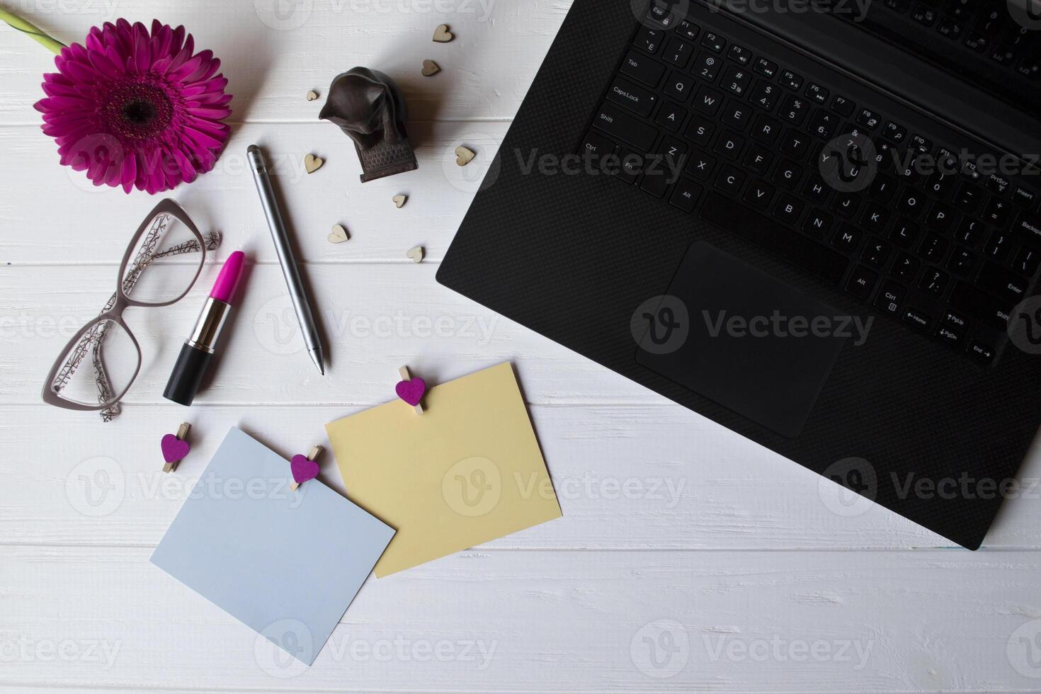 computadora portátil, vistoso memorándum hojas, los anteojos, aguja, rosado gerbera y elementos de decoración en un blanco de madera trabajo escritorio. hermosa hembra lugar de trabajo parte superior vista. foto