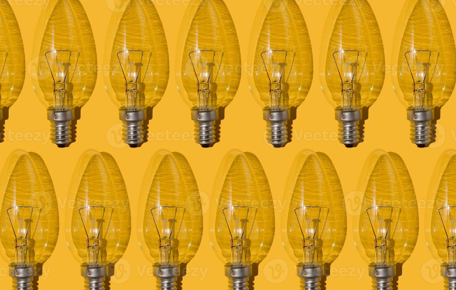 Yellow background. Electric light bulbs pattern. An old glass electric light bulb with a tungsten filament. The concept of electricity consumption and saving. photo