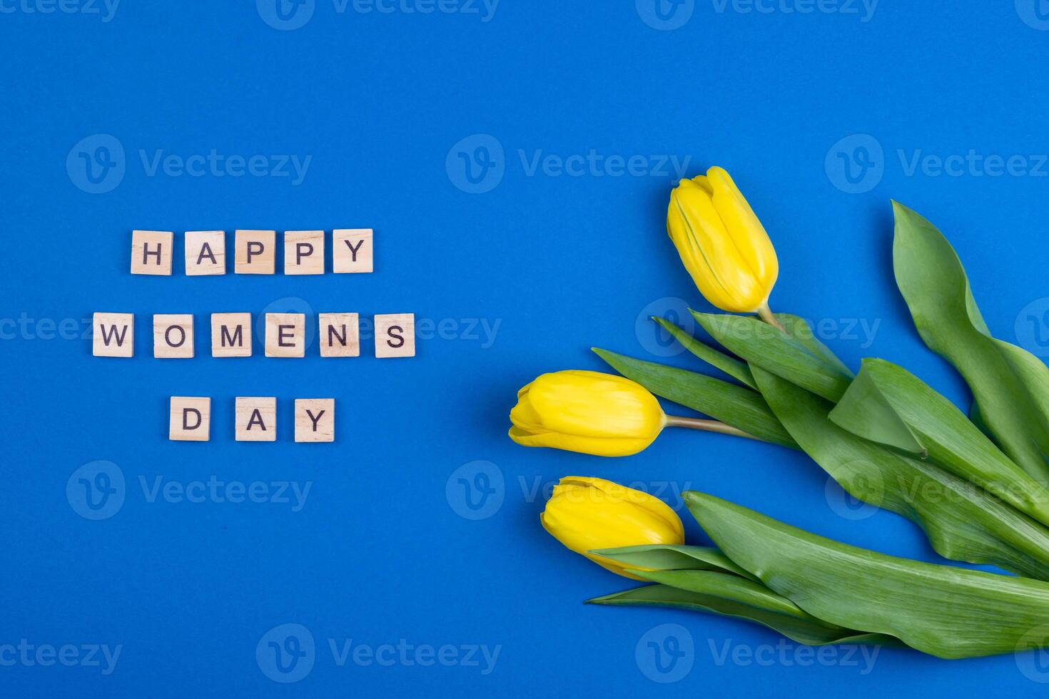 Happy womens day card. Wooden letters. Three yellow spring tulips flowers. Background with flowers tulips close-up. Gift. Blue background. Simple bouquet photo