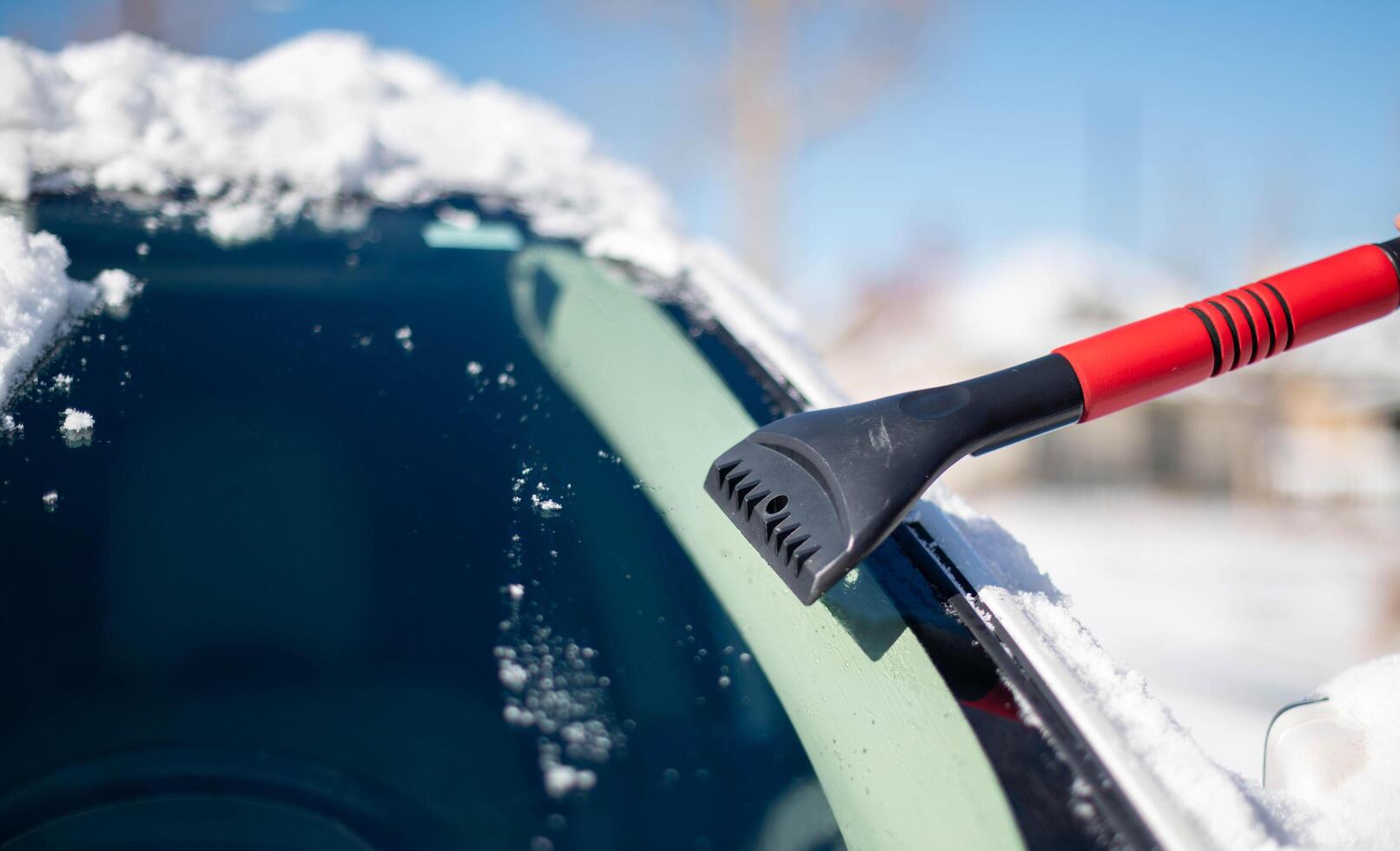 A young man wearing black warm suit for cleans his car after a snowfall on a sunny, frosty day. Cleaning and clearing the car from snow on a winter day and a severe snowstorm in winter. photo