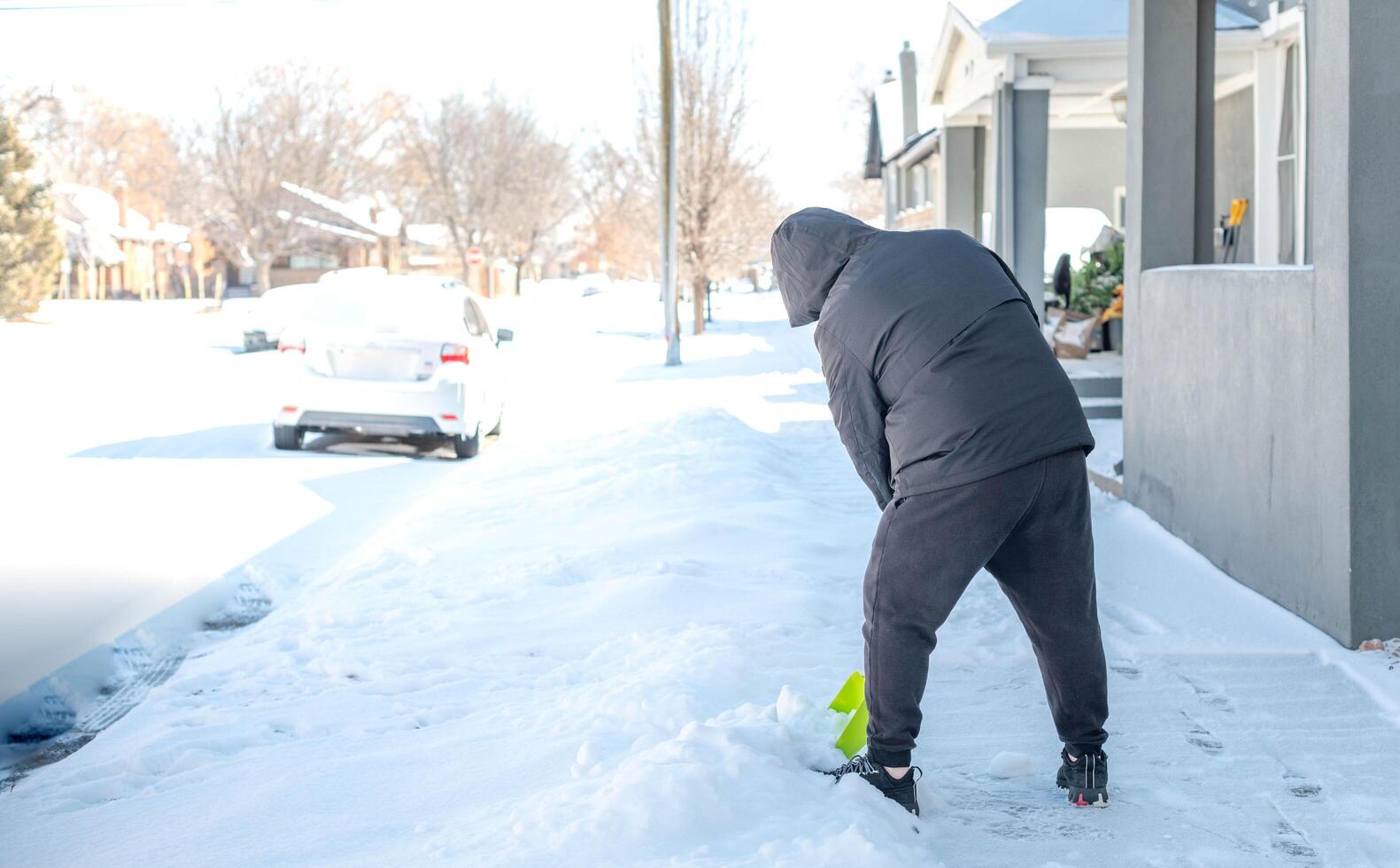 A man in a warm black jacket and trousers shoveling snow in front of their home for prepare the road for convenience. photo