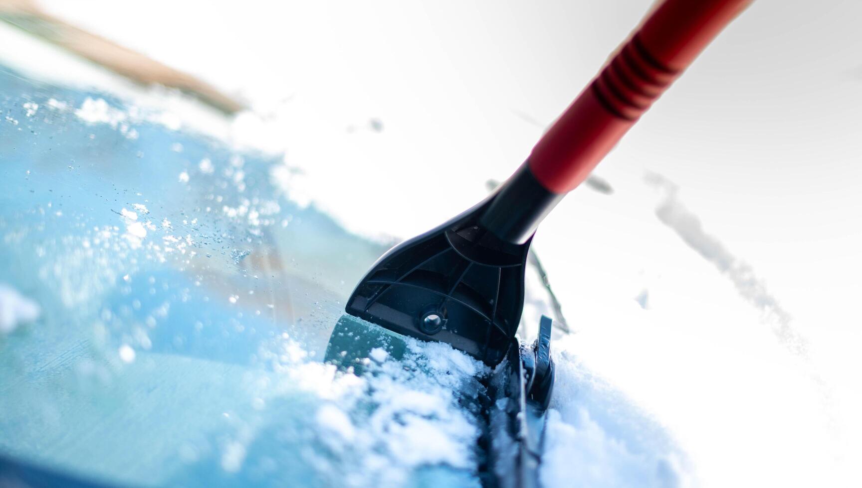 A young man wearing black warm suit for cleans his car after a snowfall on a sunny, frosty day. Cleaning and clearing the car from snow on a winter day and a severe snowstorm in winter. photo