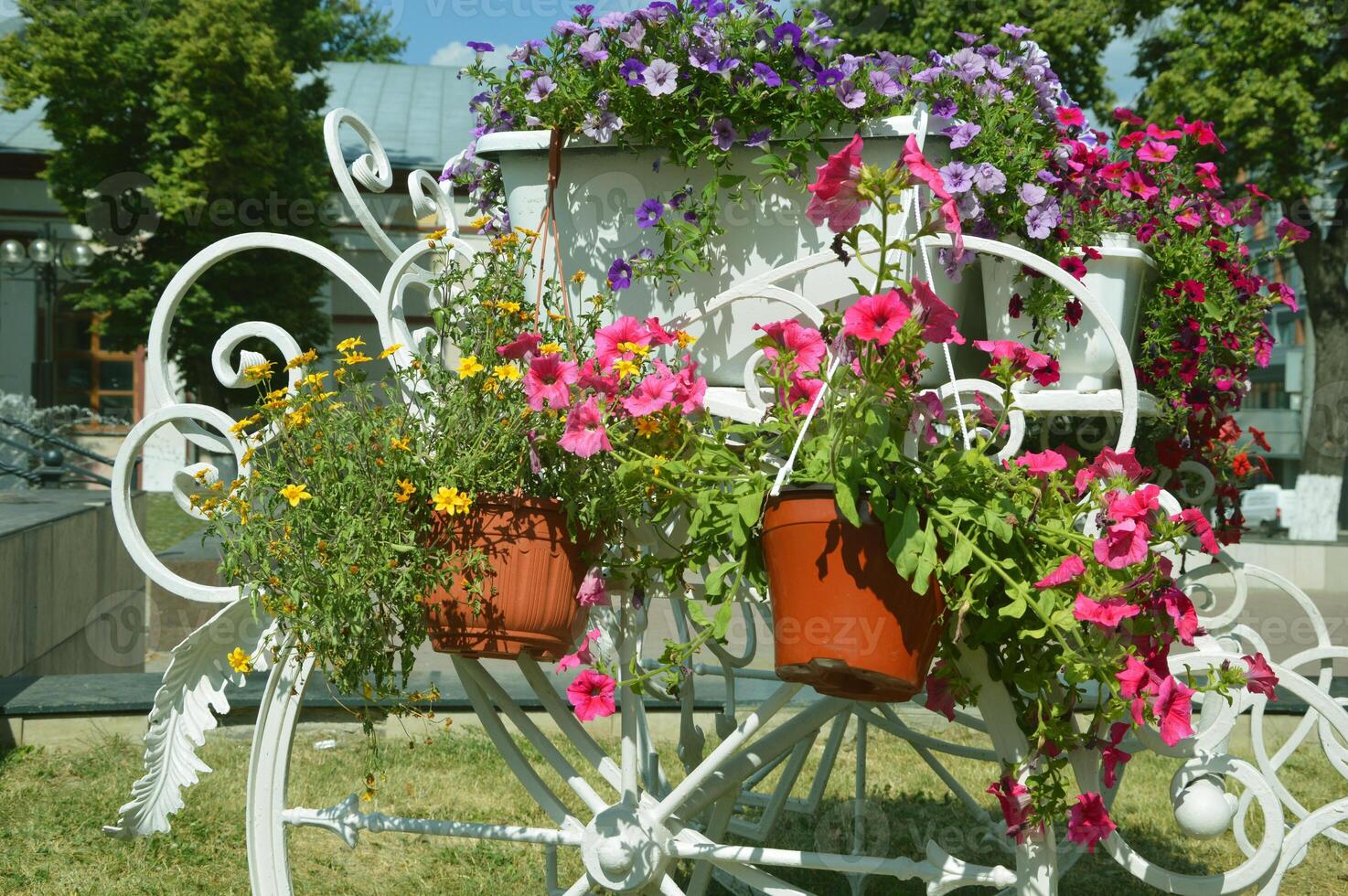 A beautiful white metal cart - a carriage or horse-drawn horse with large wheels with petunias flowers on the street, a decorative flowerbed in the summer in the city. photo