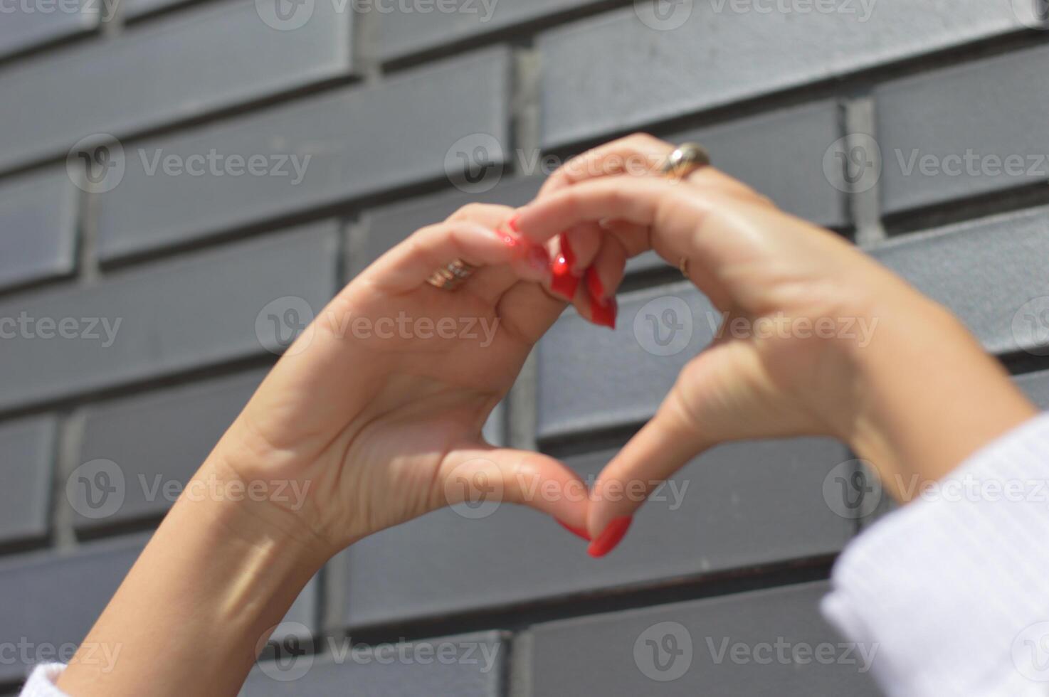 Heart folded by female hands with red nails against a gray brick wall. Valentine's Day. photo