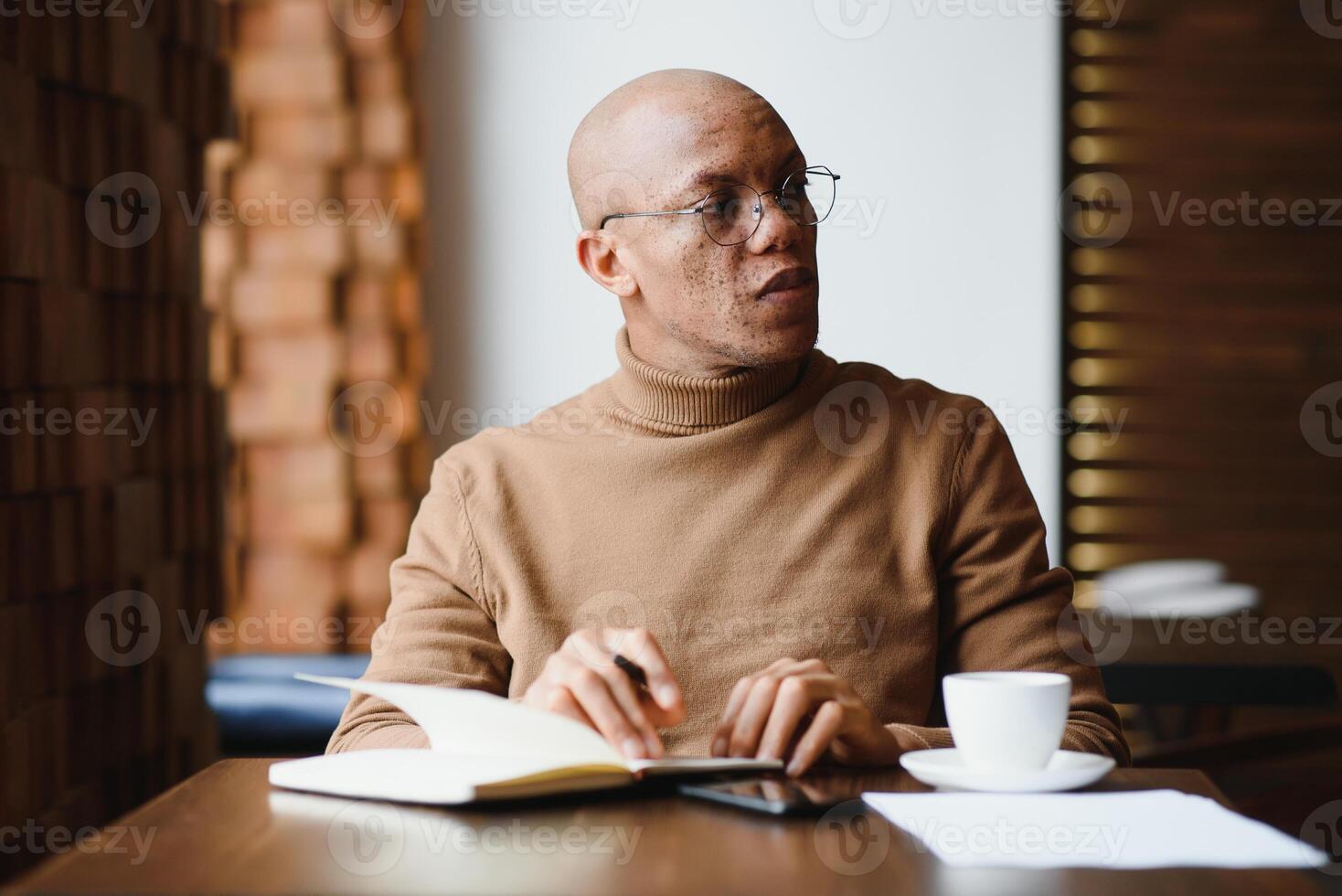 Planning The Day. Calm black student writing his lesson schedule in notebook, sitting in modern bar, empty space. photo