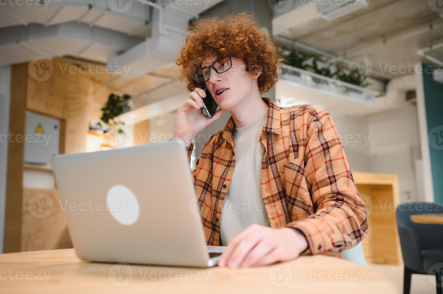 Cheerful male freelancer making telephone call share good news about project working in cafe interior,happy hipster guy having smartphone conversation while studying in good mood writing in planner photo