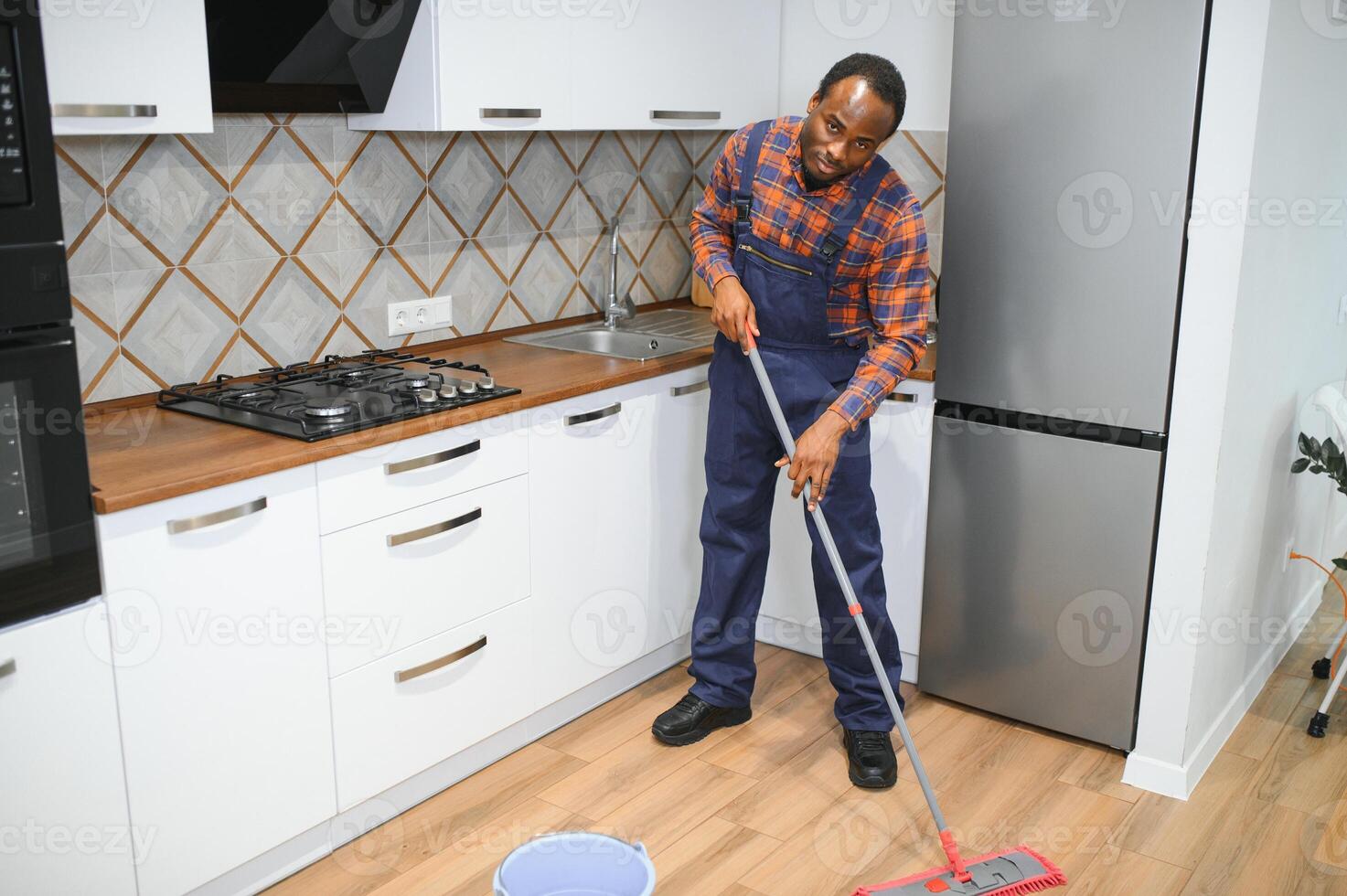 Professional cleaner in blue uniform washing floor and wiping dust from the furniture in the living room of the apartment. Cleaning service concept photo