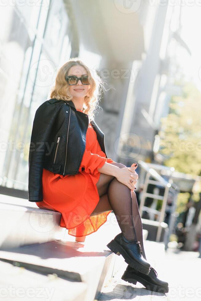 fashion portrait of young beautiful stylish woman walking in city street in red coat, style trend, drinking coffee. photo