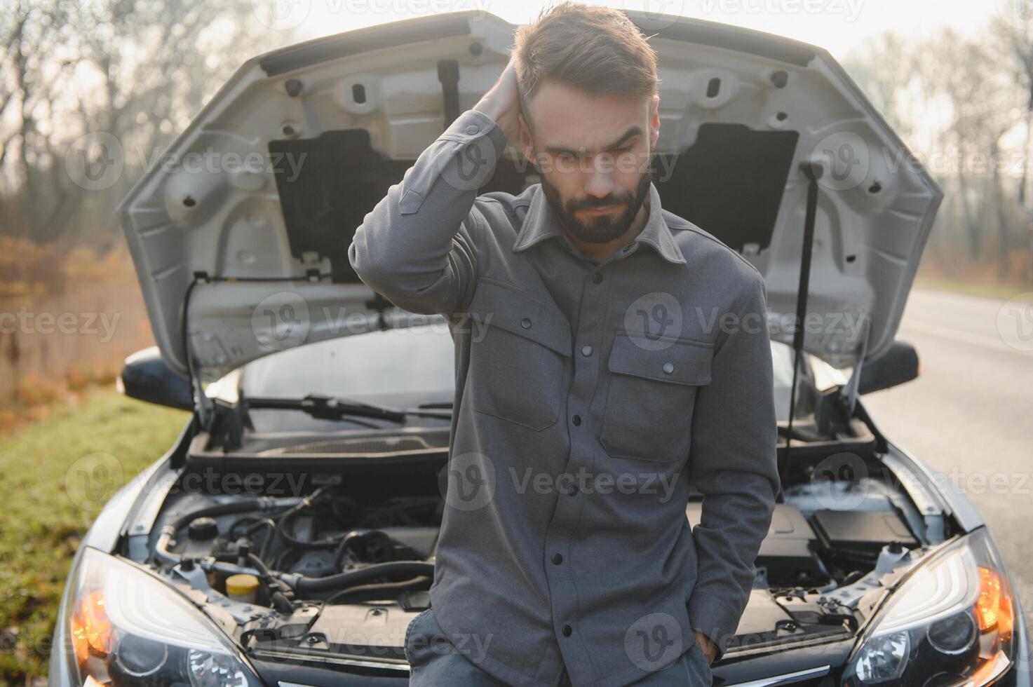 Sad driver holding his head having engine problem standing near broken car on the road. Car breakdown concept photo