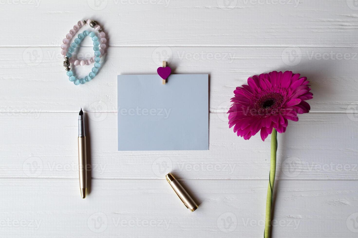 azul memorándum hoja, bolígrafo y gerbera en un blanco de madera escritorio. foto