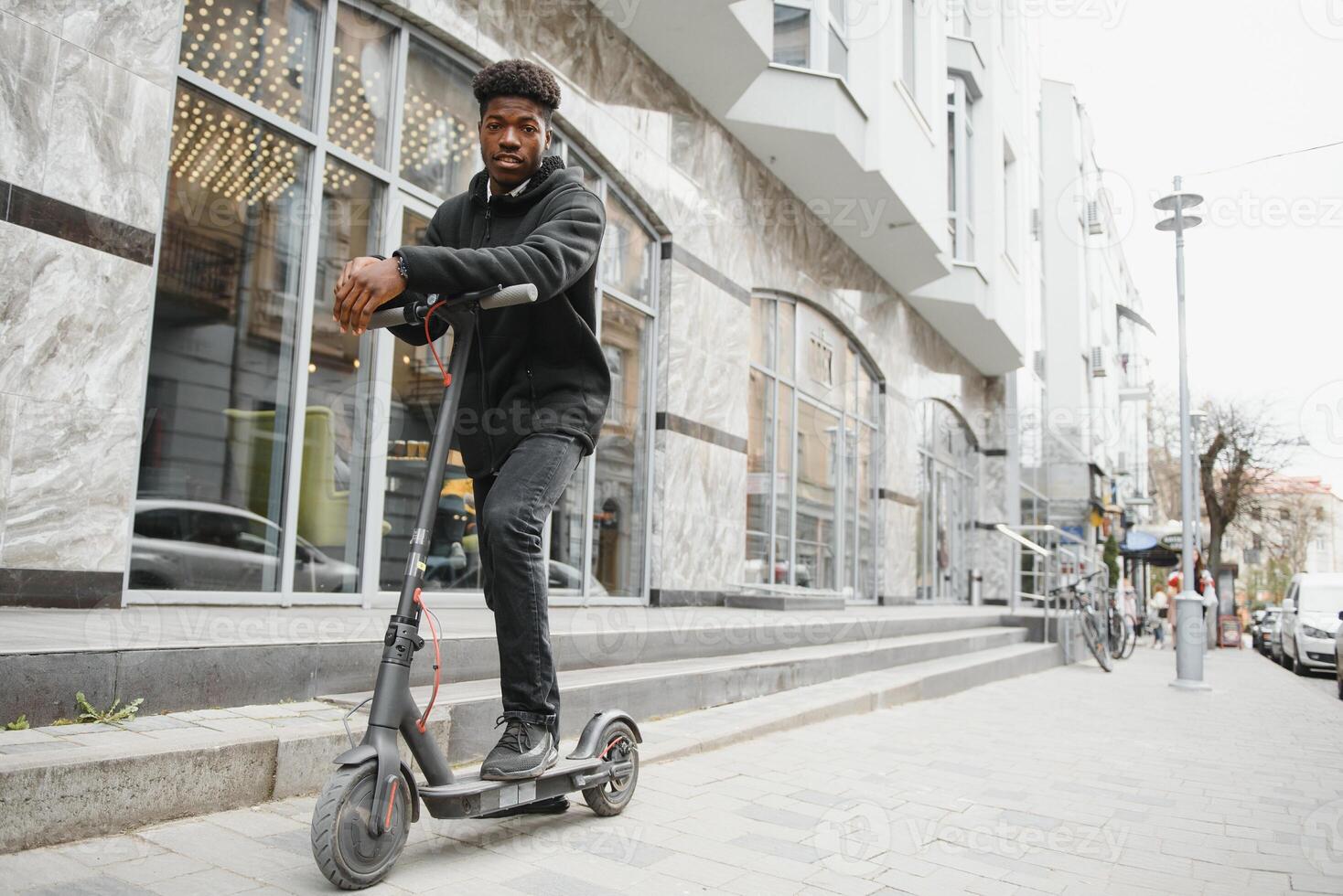 afro americano chico paseos un eléctrico scooter en contra el antecedentes de un muro, un estudiante usos eco transporte foto