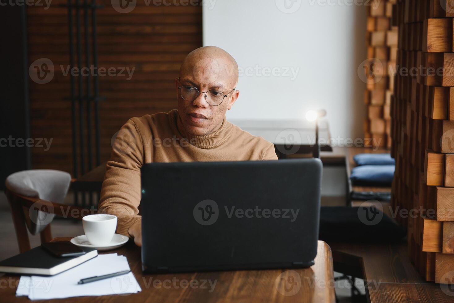 Confident prosperous African-American young top-manager wearing formal shirt having coffee and doing paperwork, working on generic laptop, using free wireless internet connection at restaurant. photo