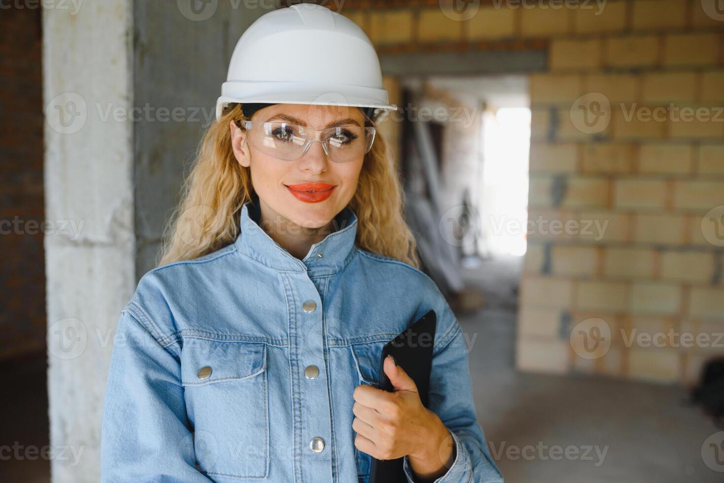 Construction concept. Pretty female builder in overalls and helmet working on construction site. photo