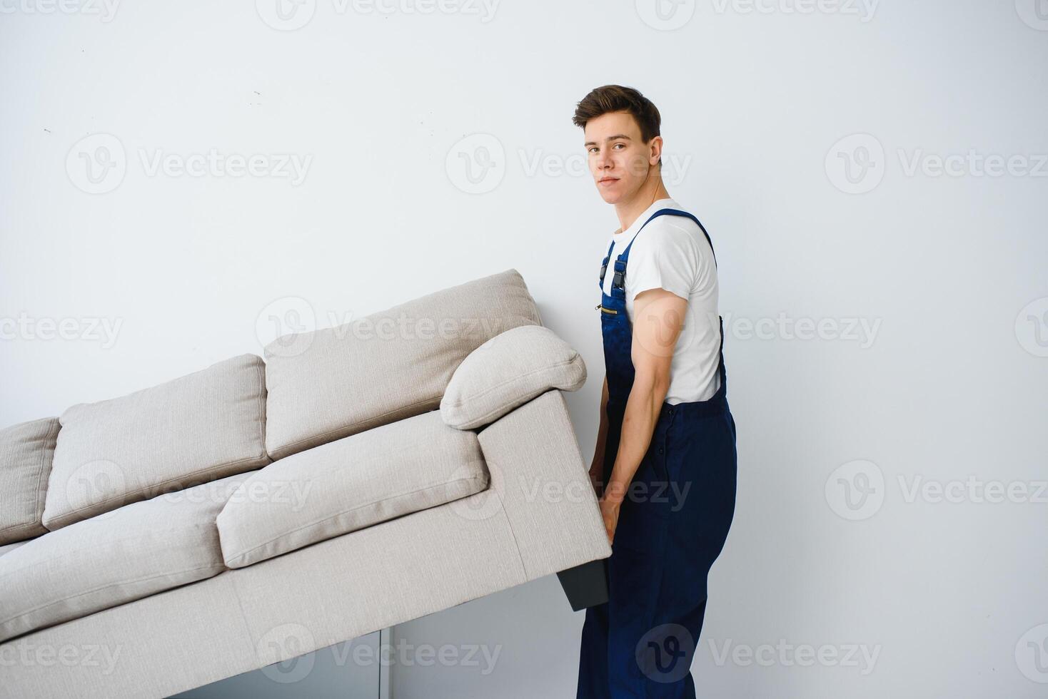 Loader moves sofa, couch. worker in overalls lifts up sofa, white background. Delivery service concept. Courier delivers furniture in case of move out, relocation. photo