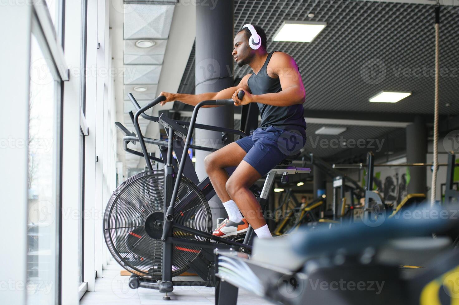 Athletic black man doing cardio workout on exercise bike in gym. Concept of sport and healthy lifestyle photo