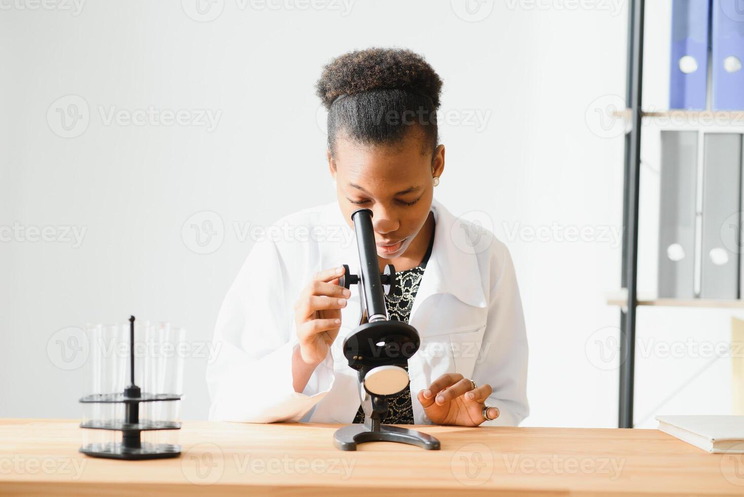 african american female lab technician looking through microscope in lab. photo