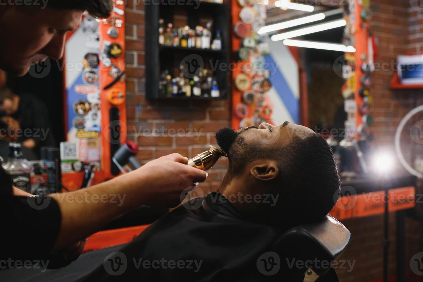 un Barbero es yendo mediante el eléctrico corte y afeitado máquina para el barba de un afroamericano brasileño chico. foto