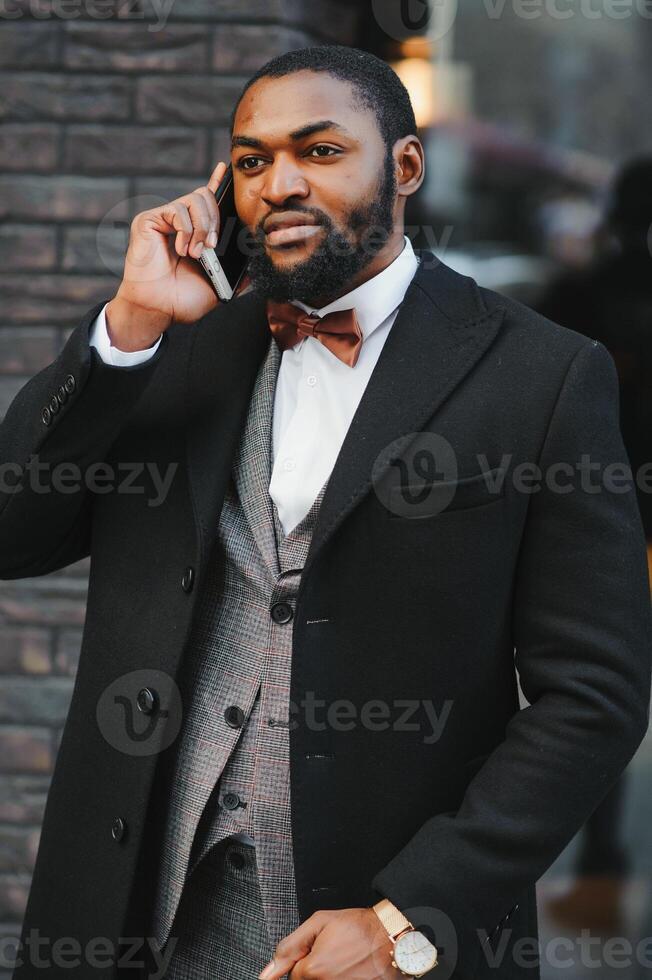 Business communications. Happy young African man in formal wear talking on the mobile phone and smiling while standing outdoors photo