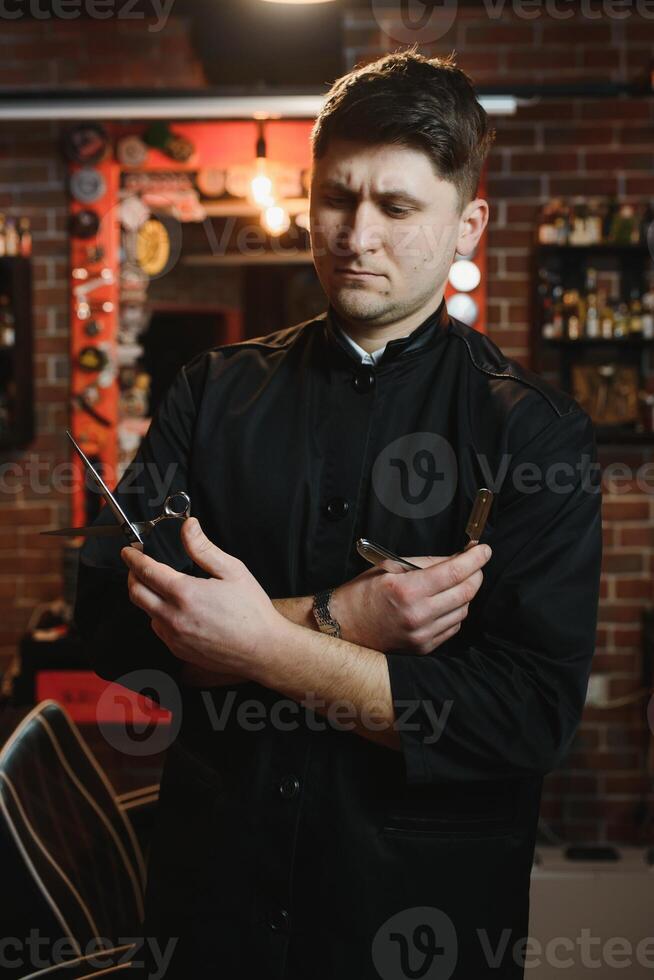 Portrait of handsome young man standing at barber shop. Stylish hairstylist standing in his salon with his arms crossed. photo