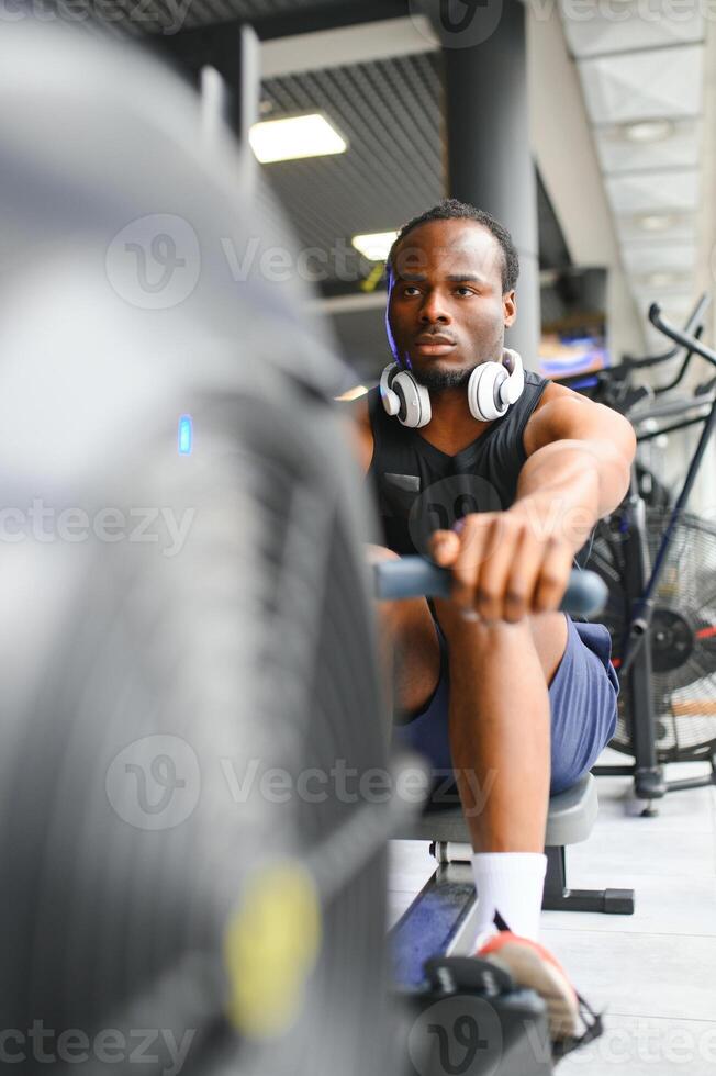 Motivated young black sportsman having workout on rowing machine photo