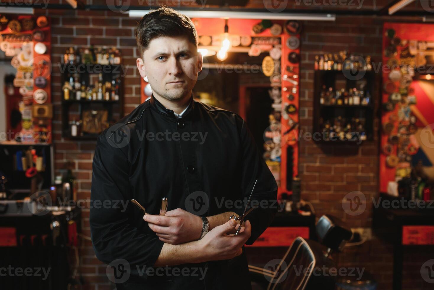 Portrait with copy space, empty place of virile harsh barber having his arms crossed, holding equipments in hand, looking at camera, isolated on grey background photo