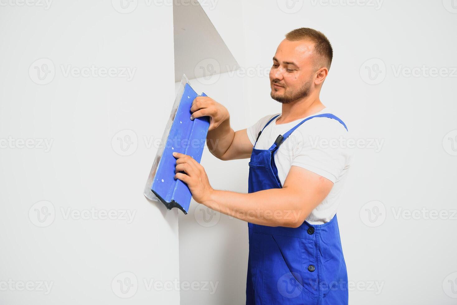 The builder carefully corrects the irregularities of the wall with a trowel. Builder in work clothes against a gray wall. Photo plasterer at work.