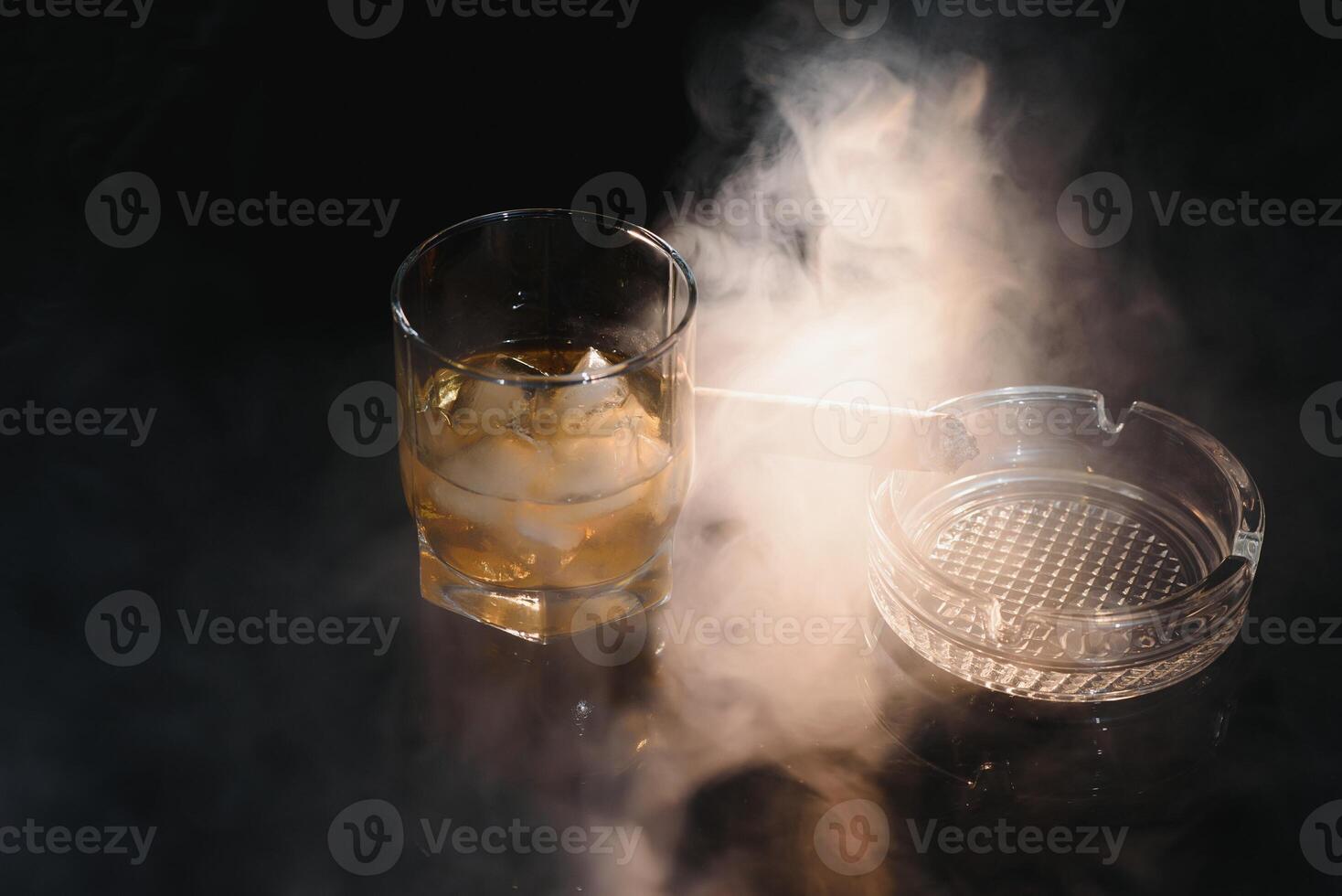 Glass of cold whiskey with cigar on dark background photo