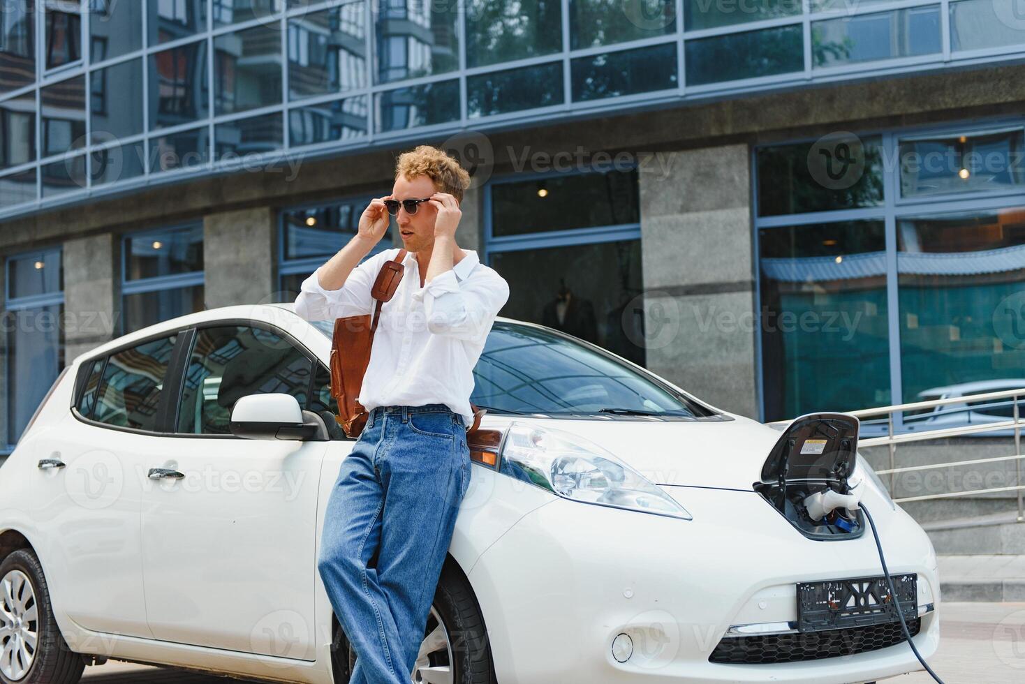 linda joven hombre cerca un moderno eléctrico coche. el concepto de ecológico transporte. foto