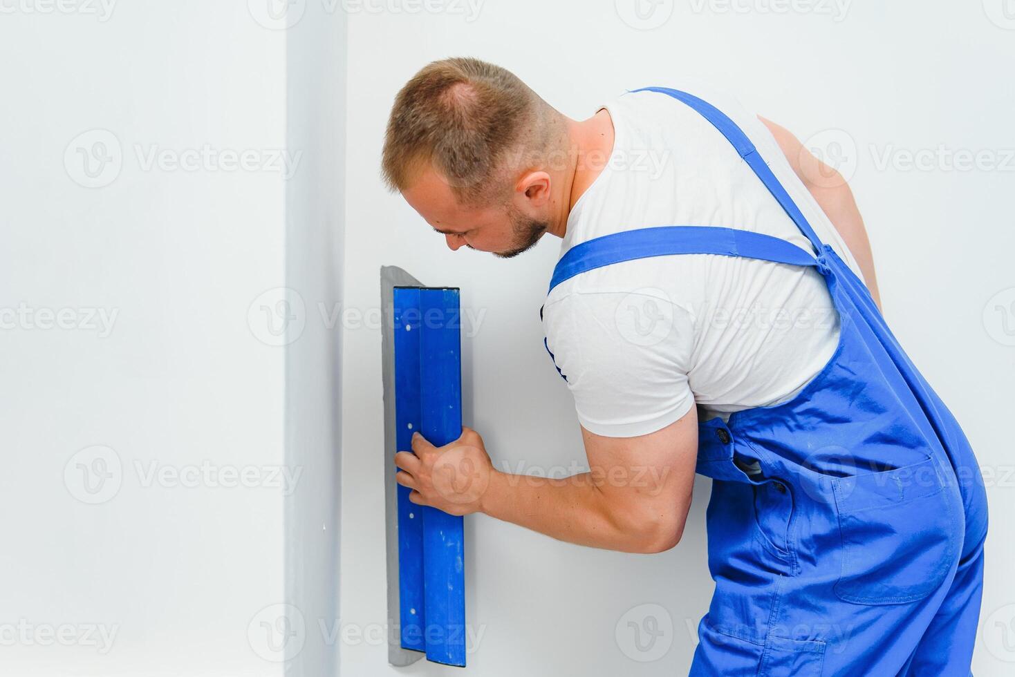 Portrait of a worker in overalls and holding a putty knife in his hands against the plastered wall background. Repair work and construction concept photo