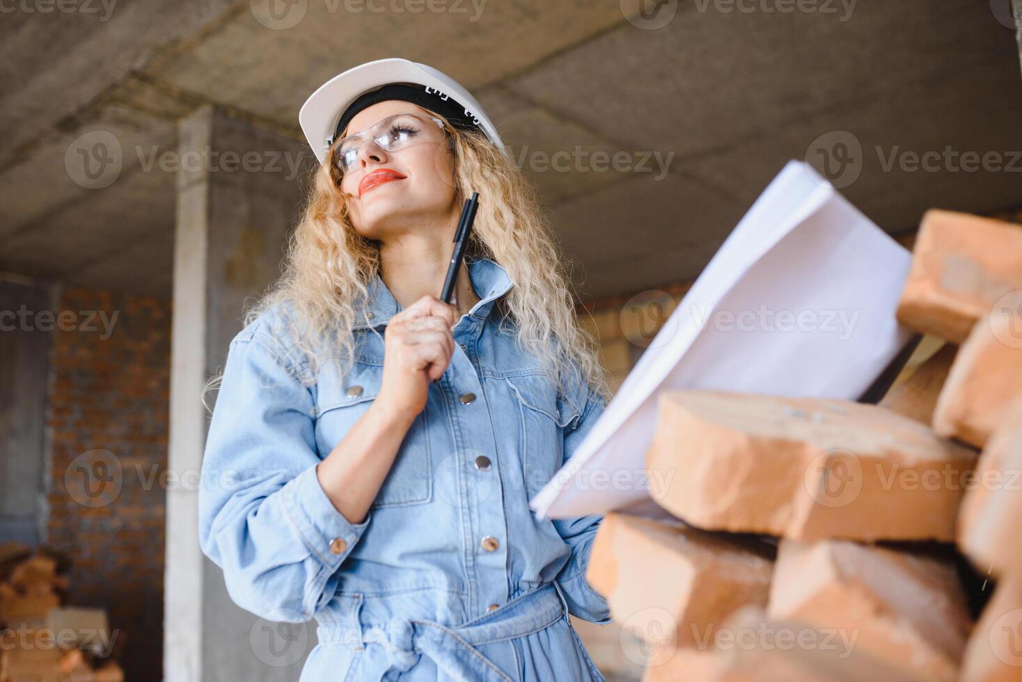 Construction concept. Pretty female builder in overalls and helmet working on construction site. photo