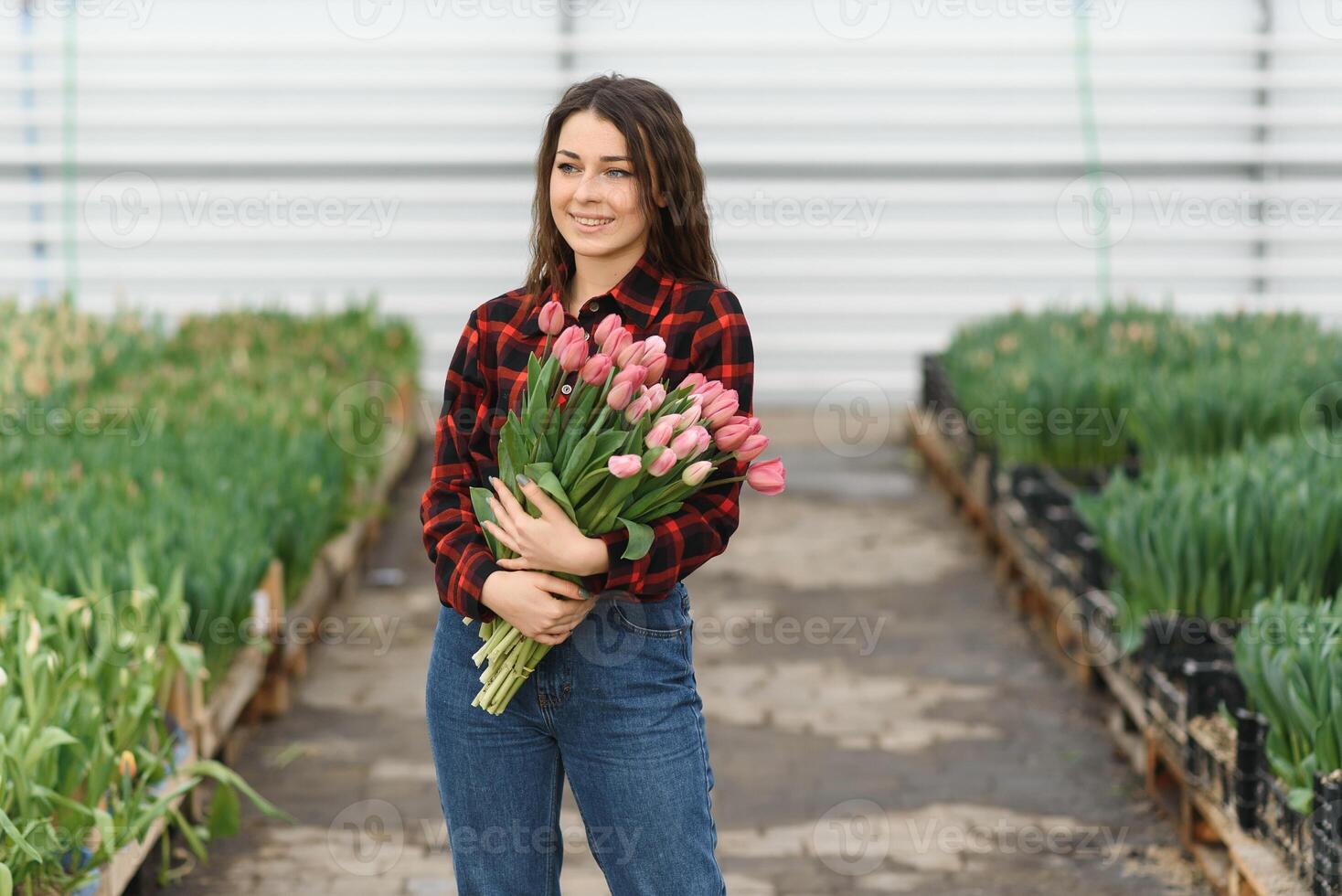 Young beautiful woman greenhouse worker holds a blooming tulips in her hands and smiles. photo