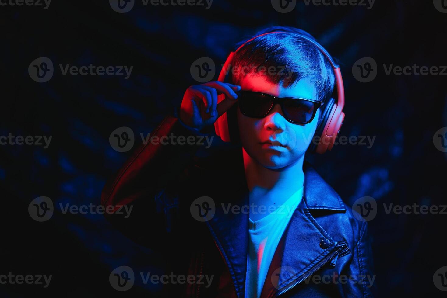 teen boy listening to music with headphones, neon light trending portrait. Looks at the camera photo