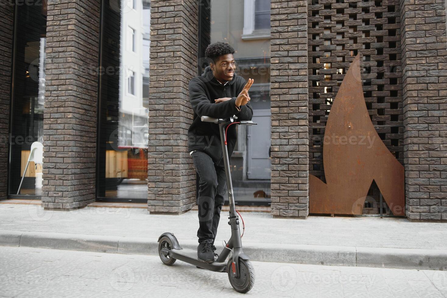 Active Leisure Concept. Side view of black male student driving stand-up scooter over brick road, copy space for ad or text photo