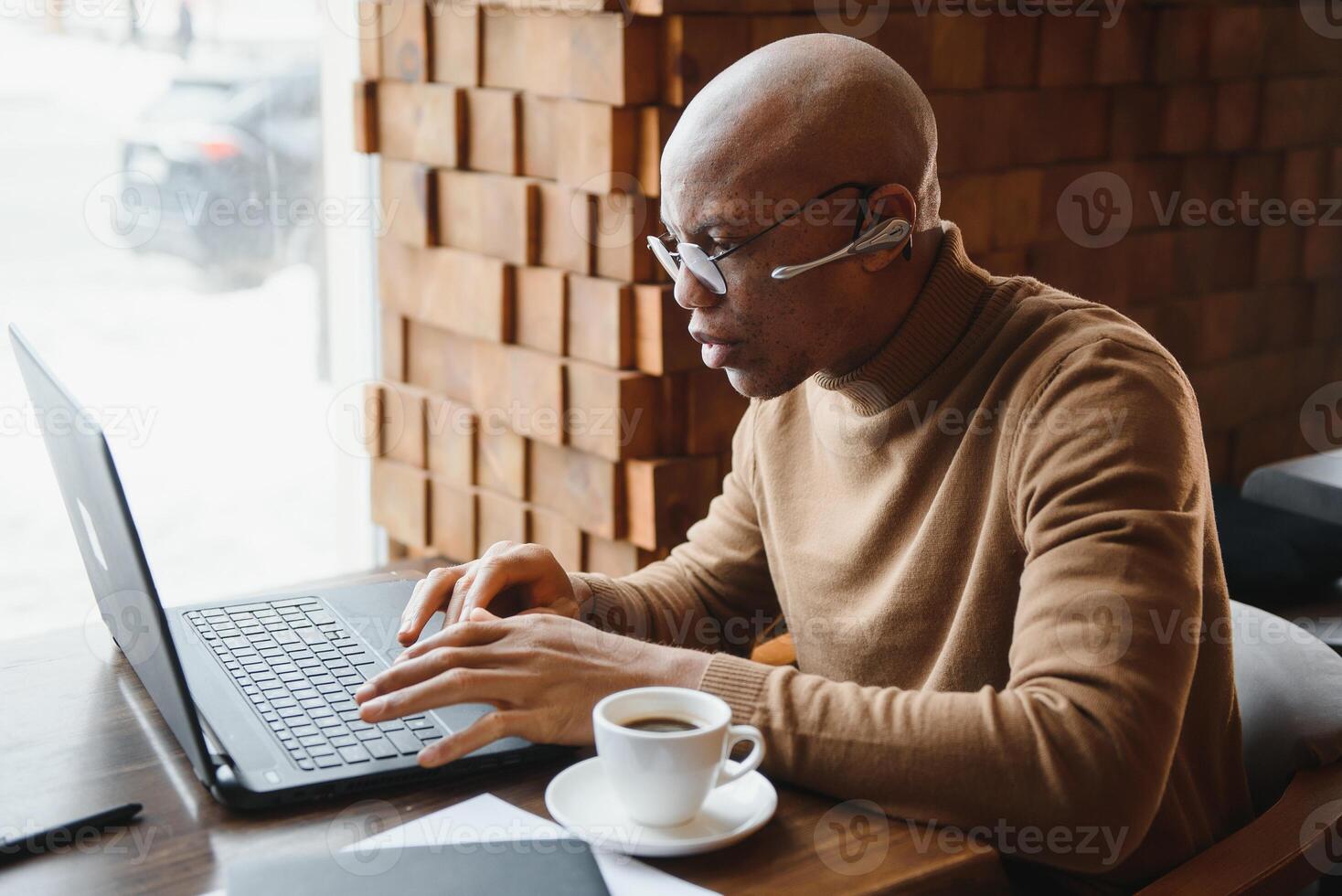 Portrait of smiling African American man in glasses sit at desk in office working on laptop, happy biracial male worker look at camera posing, busy using modern computer gadget at workplace. photo