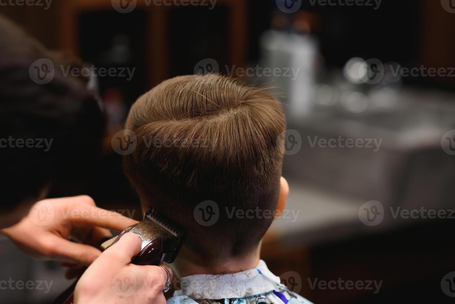 A little cute boy sits in a hairdresser's at the stylist's, a schoolchild is getting hair cut in a beauty salon, a child at a barbershop's, a short men's haircut photo