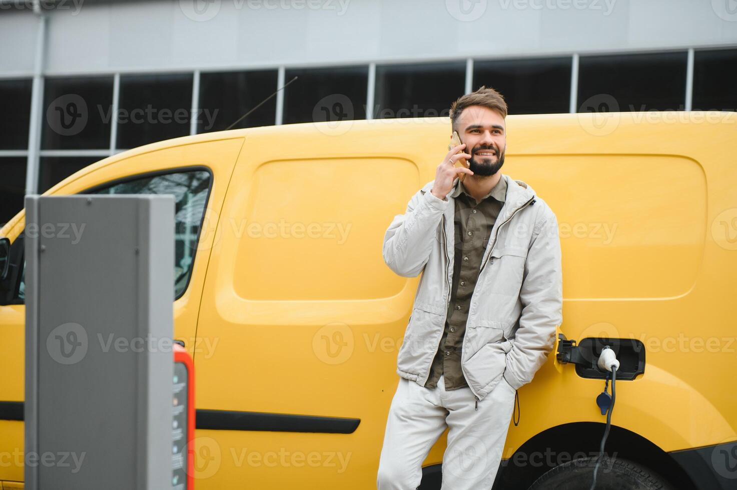 Casual man near electric car waiting for the finish of the battery charging process photo