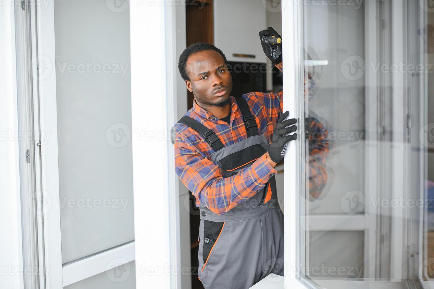 Workman in overalls installing or adjusting plastic windows in the living room at home photo