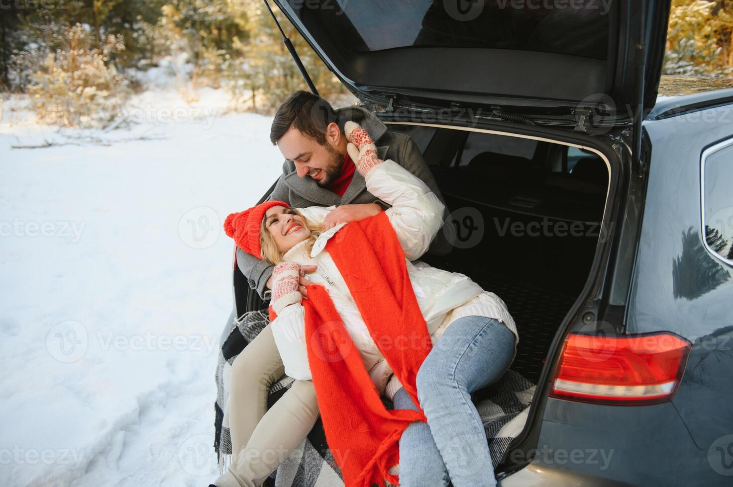 Smiling together. Nice couple have weekend at countryside at winter time. Sitting on the rear part of modern car. photo