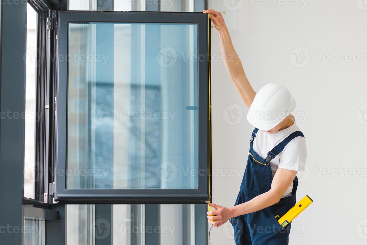 Workman in overalls installing or adjusting plastic windows in the living room at home photo