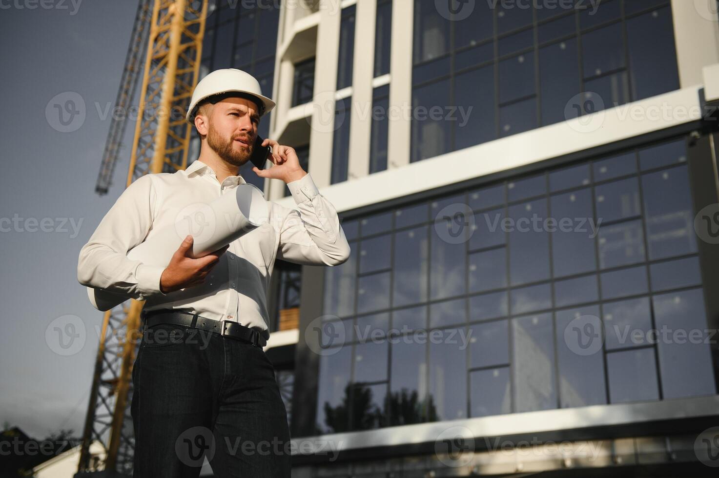 Engineer next to building cranes. Concept - large construction project. Architect directs the construction process. Drawings and tablet in the hands. photo