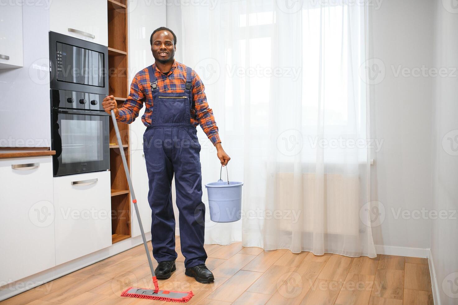 joven africano hombre lavados el piso con un fregona en el habitación foto