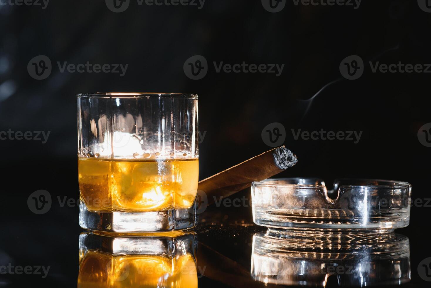 A glass of whiskey or Bourbon with ice cubes and a cigar on a black slate with smoke photo