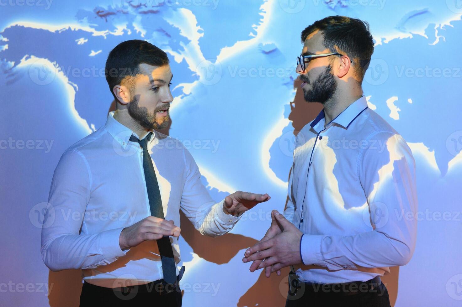 Two attractive young european businessmen on digital map blue background. Communication, teamwork and network concept photo