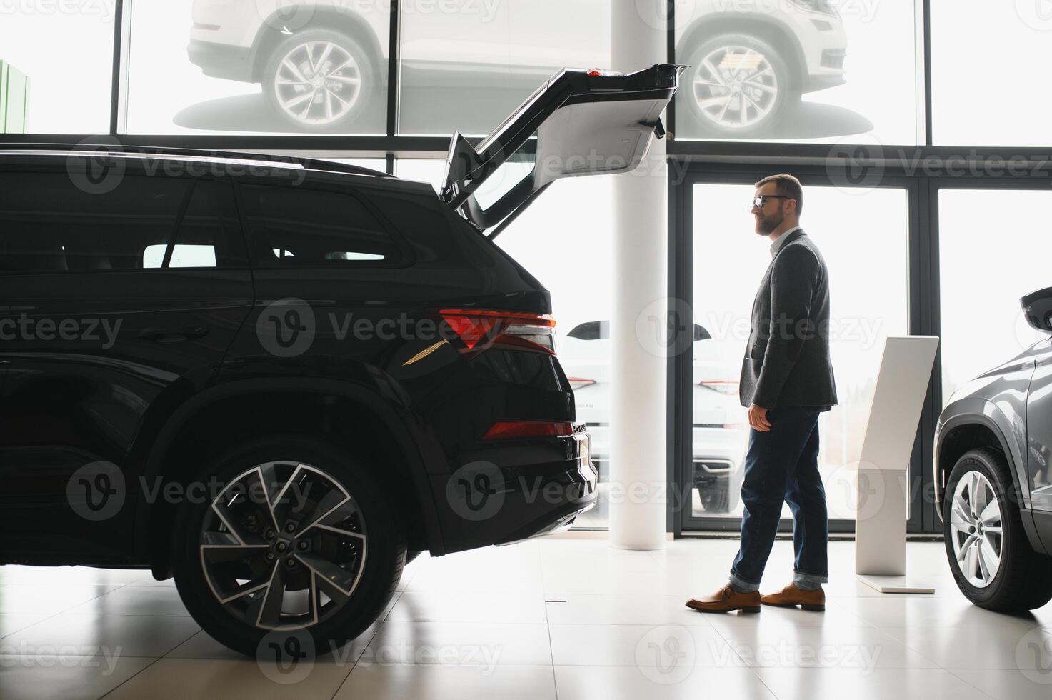 Visiting car dealership. Handsome bearded man is stroking his new car and smiling photo