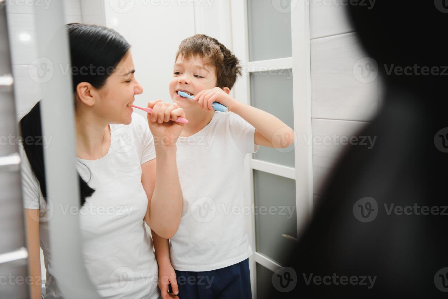 hermosa madre y contento hijo cepillado dientes cerca espejo en baño foto