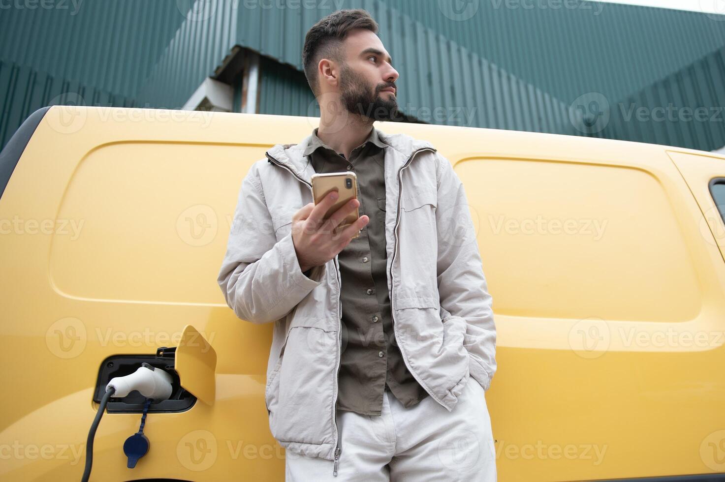 Casual man near electric car waiting for the finish of the battery charging process photo