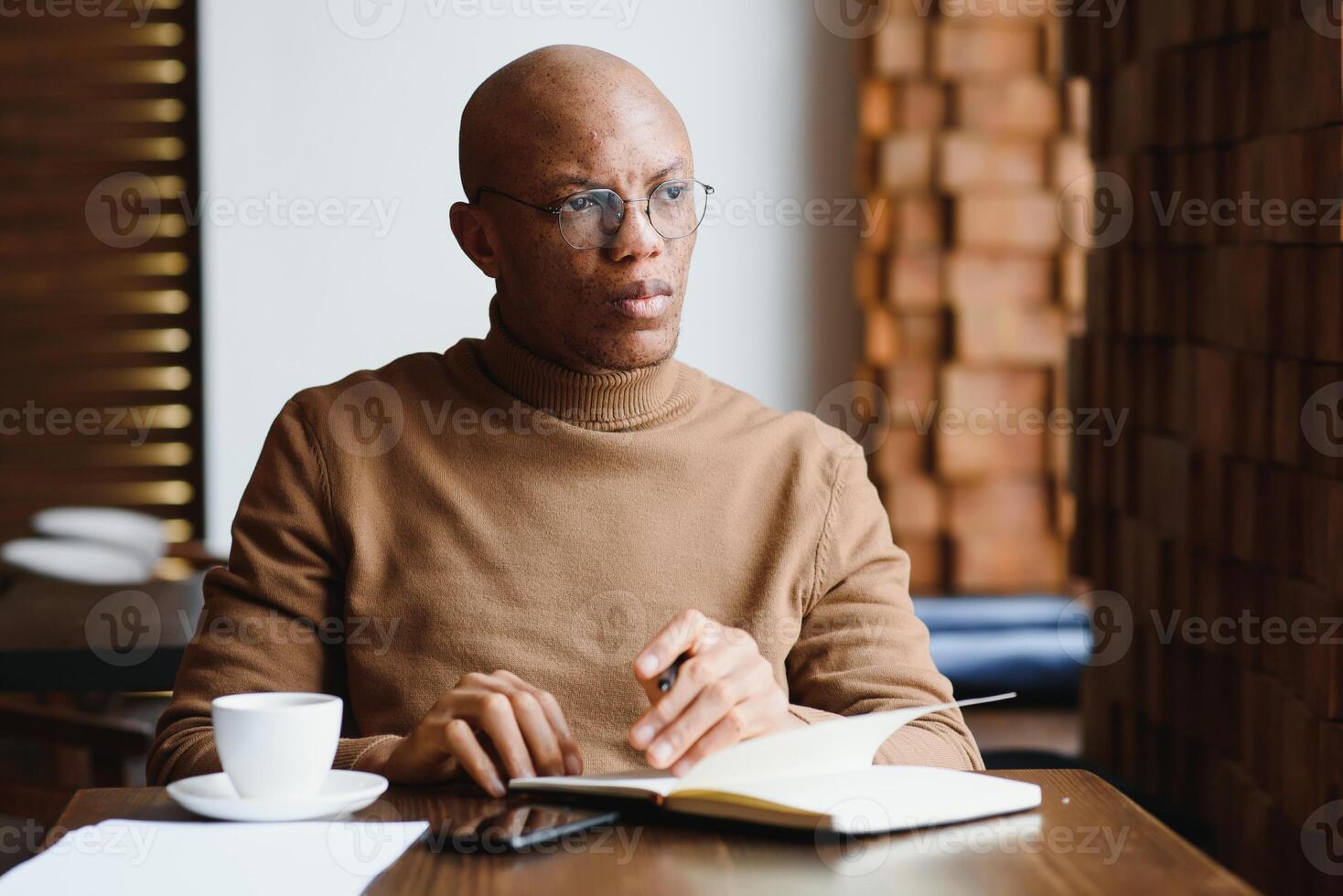 Planning The Day. Calm black student writing his lesson schedule in notebook, sitting in modern bar, empty space. photo