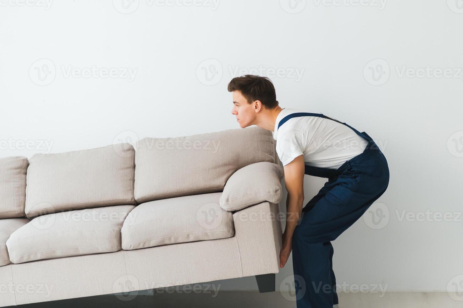 Loader moves sofa, couch. worker in overalls lifts up sofa, white background. Delivery service concept. Courier delivers furniture in case of move out, relocation. photo