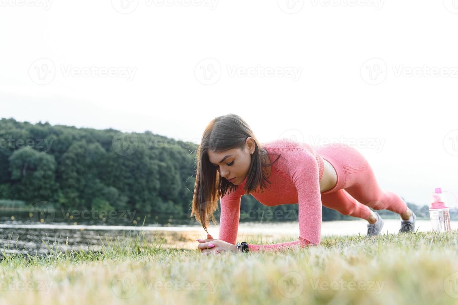 Young caucasian woman doing active training exercise on a yoga mat near the river in summer. Concept of healthy lifestyle photo